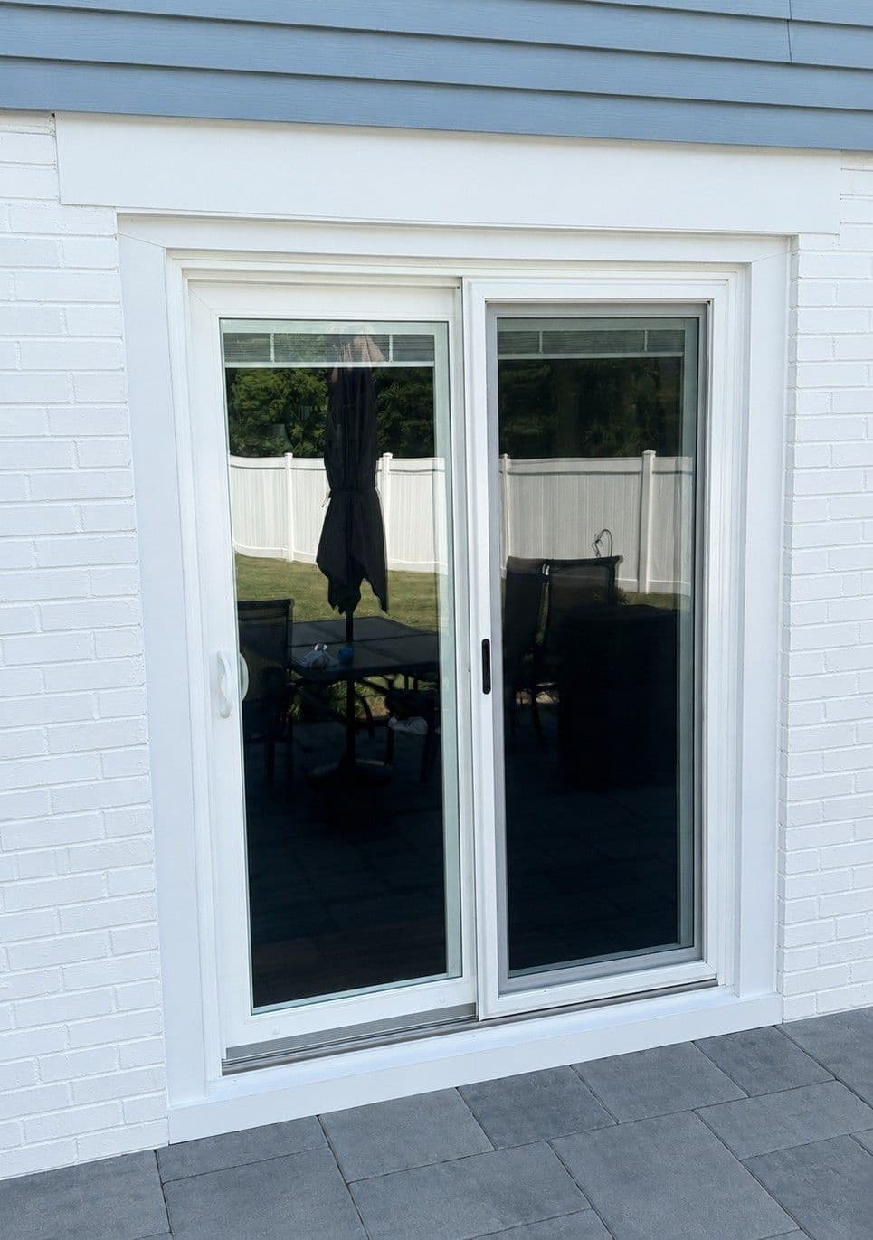 Pair of white-framed sliding glass doors opening to a patio with black umbrellas and furniture, white fence visible in background