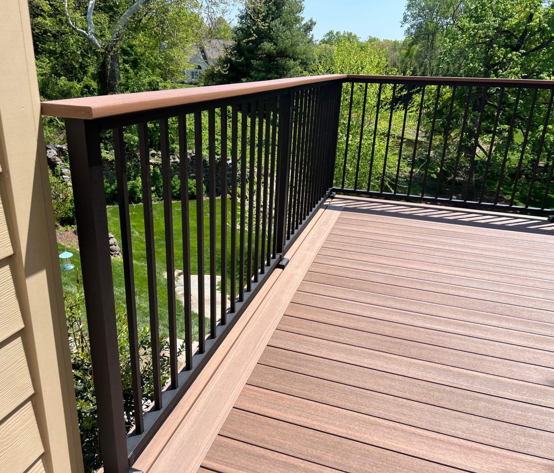 Wooden deck with black metal railing and cedar top rail overlooking wooded landscape on sunny day